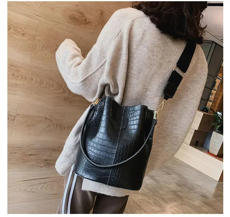 A woman wearing a beige sweater holds a black alligator pattern crossbody bag.