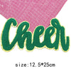 Green glitter letter patch spelling Cheer cut out on a pink grid background