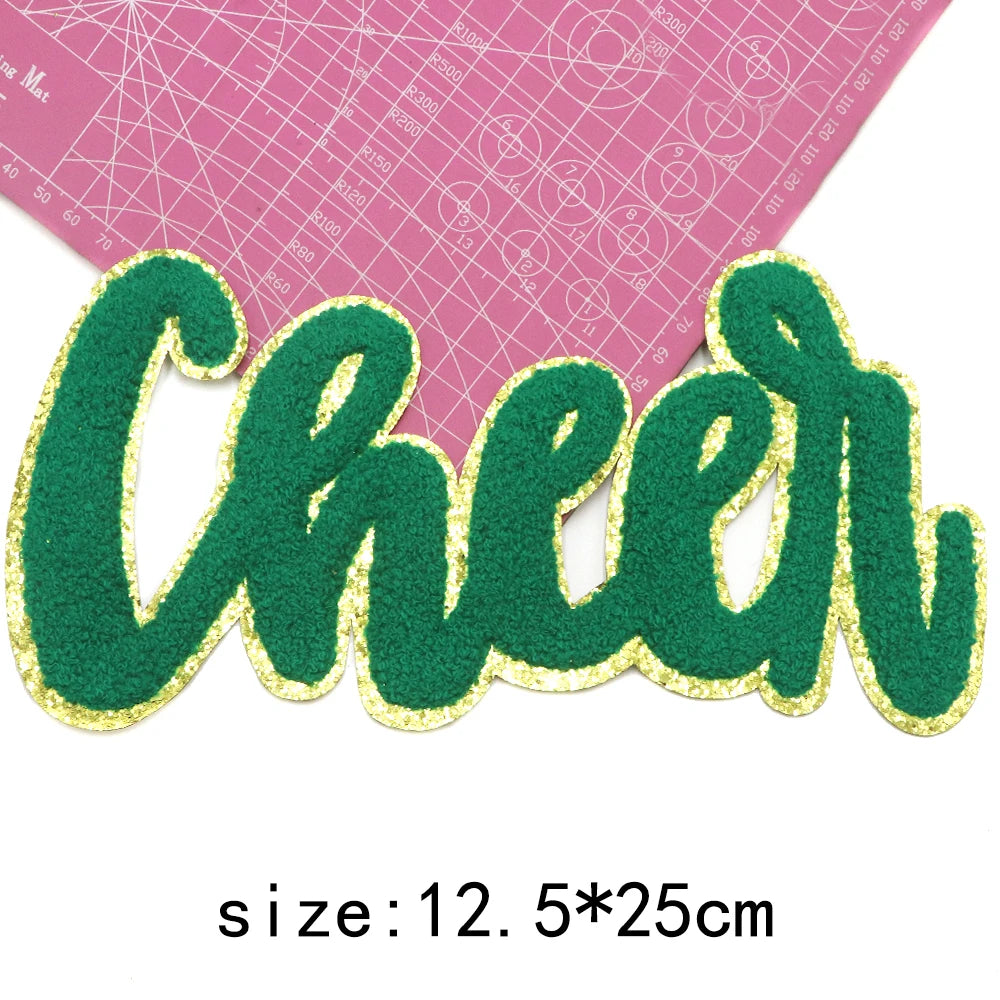 Green glitter letter patch spelling Cheer cut out on a pink grid background