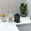 A set of clear apothecary jars with lids for storage, including a wooden jar, glass jars filled with straws, and a black jar.