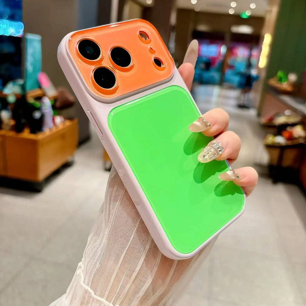 A hand holds a color blocking phone case with an orange camera window and a bright green back panel.