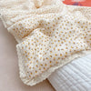 Close-up of a floral muslin baby blanket featuring yellow and white patterns, folded and displayed on a light surface.