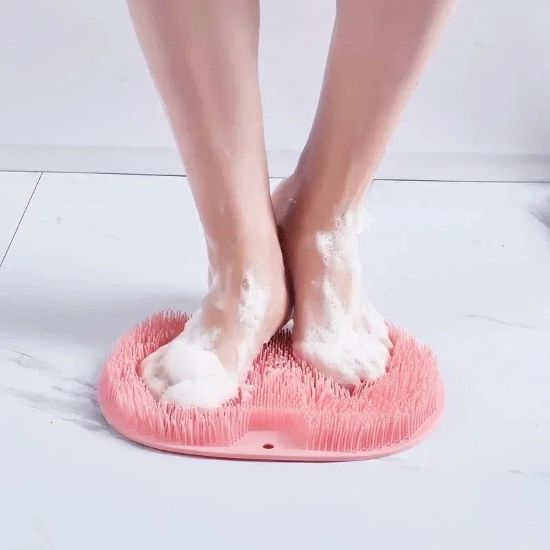 A pair of bare feet resting on a pink silicone exfoliating shower mat with bristles.