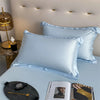 A light blue luxury bamboo flat sheet is displayed on a bed, next to a watch and a magazine.