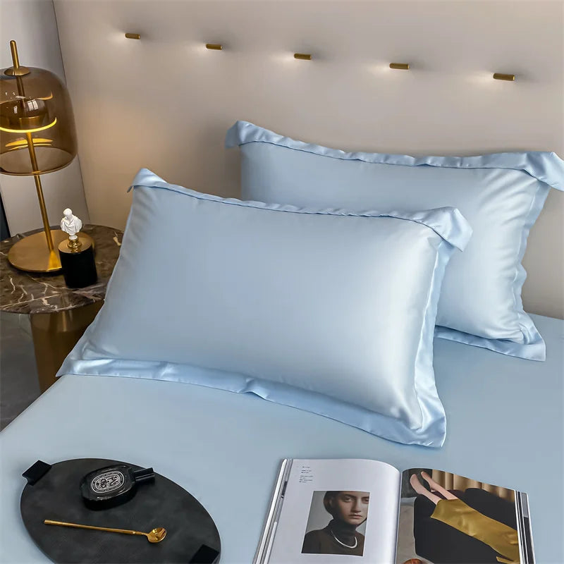 A light blue luxury bamboo flat sheet is displayed on a bed, next to a watch and a magazine.