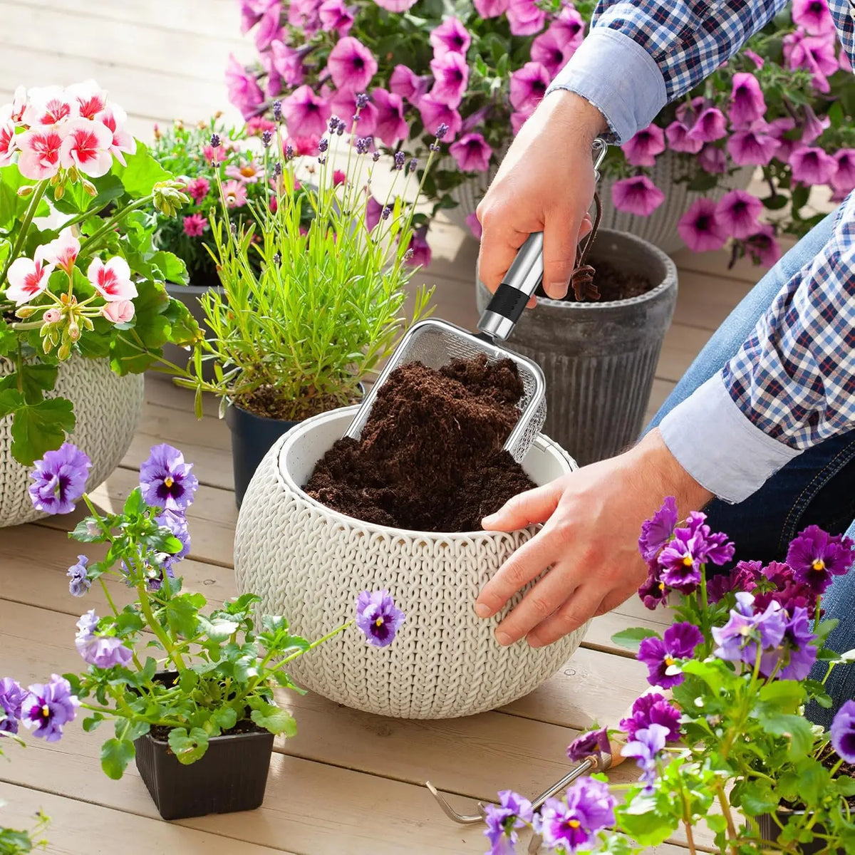 A hand is using a stainless steel soil sieve set to pour dark potting soil into a woven plant pot.