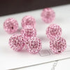 Pink crystal clay round beads scattered on a white surface for DIY jewelry and craft projects