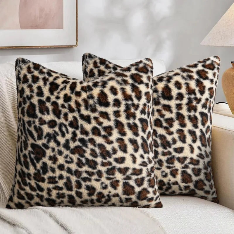 A close-up of three plush velvet leopard print pillows resting on a light-colored sofa.
