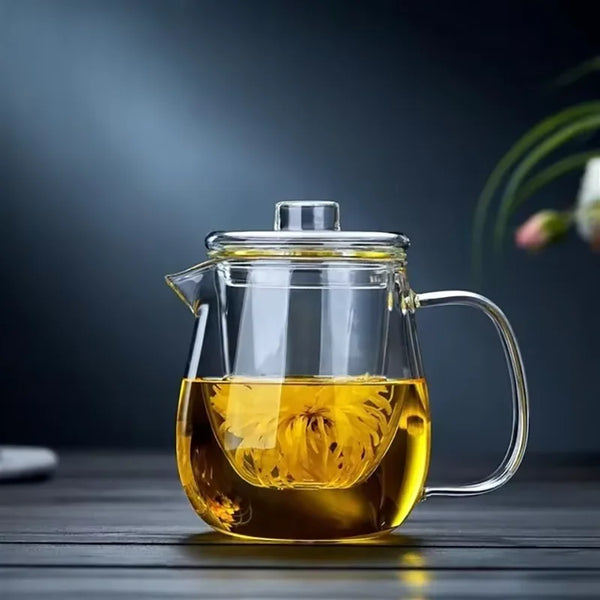 A clear glass teapot with a handle and a removable infuser filled with amber tea on a dark wooden surface.