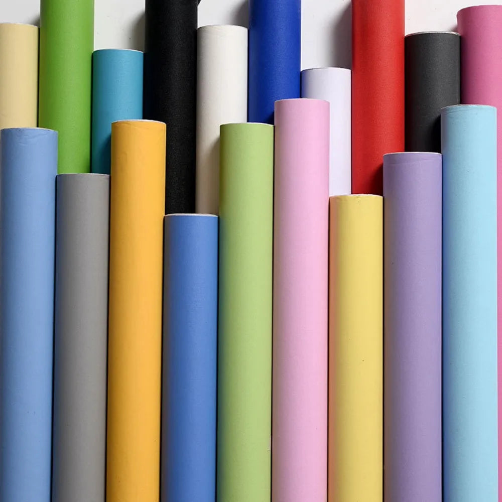 A vertical arrangement of colorful self-adhesive peel-and-stick wallpaper rolls in various shades of green, yellow, blue, pin