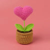 Handcrafted crochet pink heart flower with green leaves growing in a brown crocheted pot