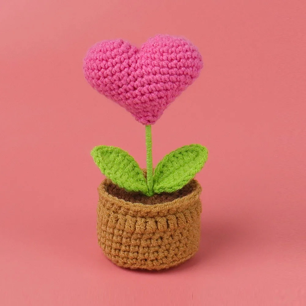 Handcrafted crochet pink heart flower with green leaves growing in a brown crocheted pot