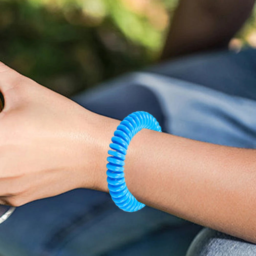 A close-up of a person's wrist wearing a bright blue, coiled mosquito repellent bracelet.