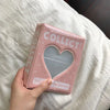 A pink mini photo album titled Collect with a heart design resting on white bedding.
