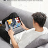 A person is relaxing on a couch watching TV with a tablet placed on an adjustable stand.