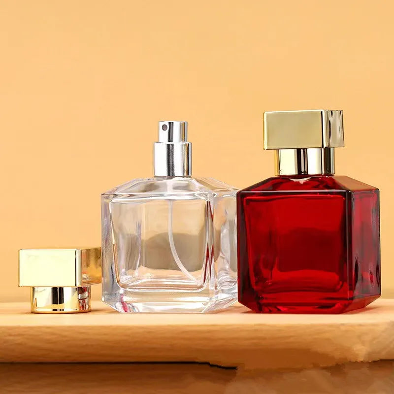 A clear glass perfume bottle with a silver sprayer and a red glass bottle next to it on a wooden surface.