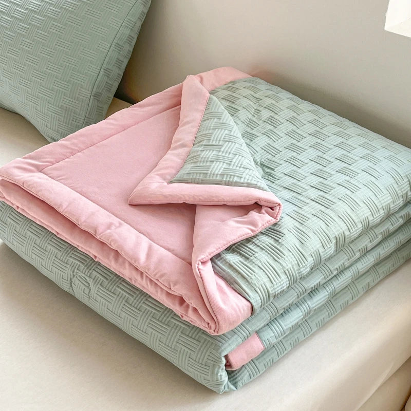 Pink and mint green breathable waffle-weave summer quilt folded on a light surface