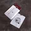 A white RFID passport sleeve is shown next to a maroon card, with another white sleeve lying below on a dark surface.