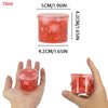 A hand holds a clear plastic container of red jelly cube slime with colorful crystals inside.