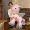 A young woman is holding a large pink unicorn plush toy with rainbow accents and a horn.