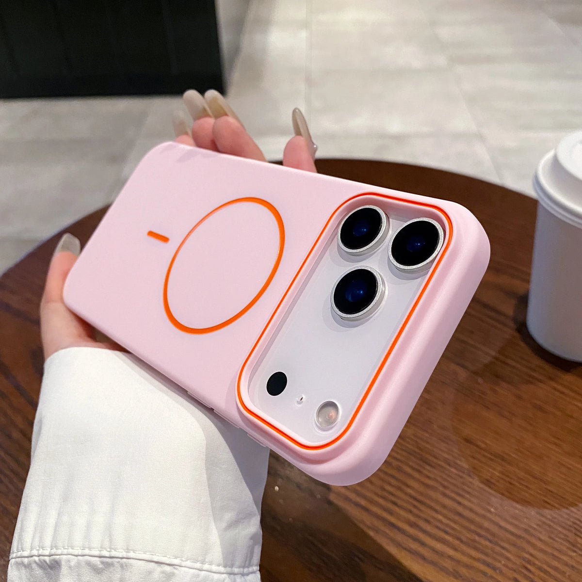 A pink magnetic phone case with MagSafe support is held by a person on a wooden surface.
