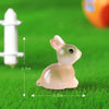 A small, translucent pink resin bunny figurine is shown on green grass next to a white object for scale.