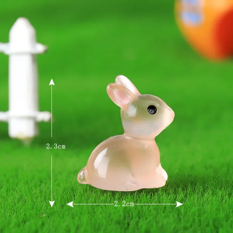 A small, translucent pink resin bunny figurine is shown on green grass next to a white object for scale.