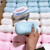 A hand is holding a light blue squishy soap shape fidget toy among many white and pink soaps.