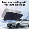 A black foldable car windshield sunshade is shown in use on a silver sedan.