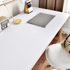 A laptop and a small orange desk accessory are placed on a white table with a wooden chair visible.