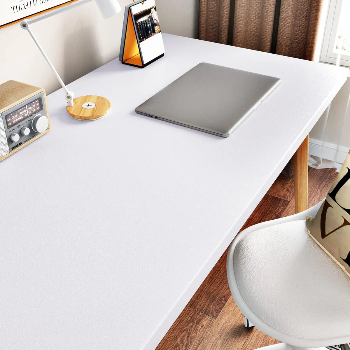 A laptop and a small orange desk accessory are placed on a white table with a wooden chair visible.