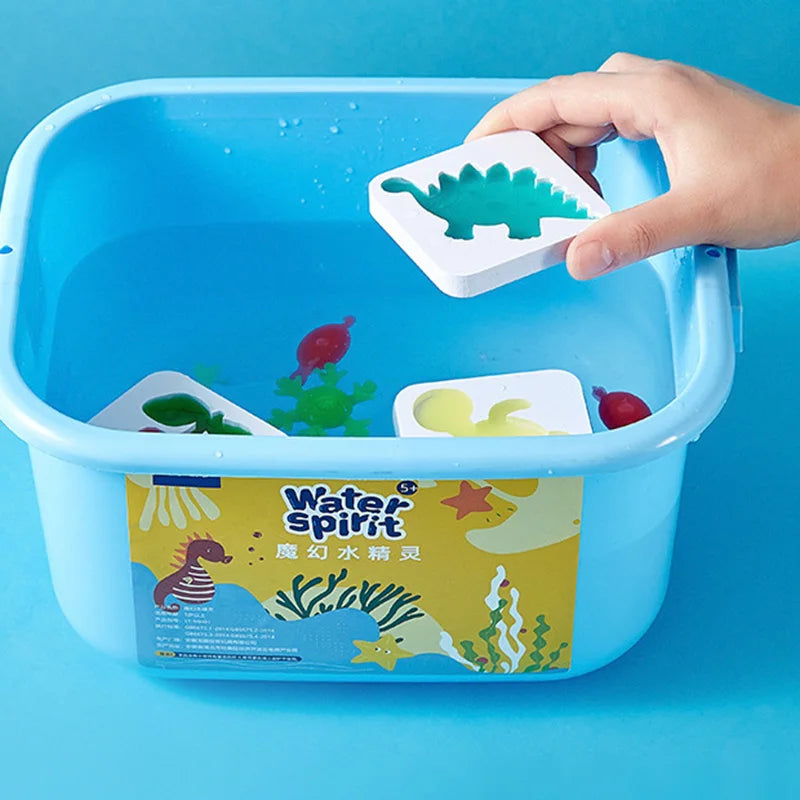 A hand places a green plastic dinosaur figure into a blue plastic container of Water Spirit craft materials.