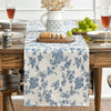 A blue floral patterned linen table runner set on a wooden table with a glass of red wine and green grapes.