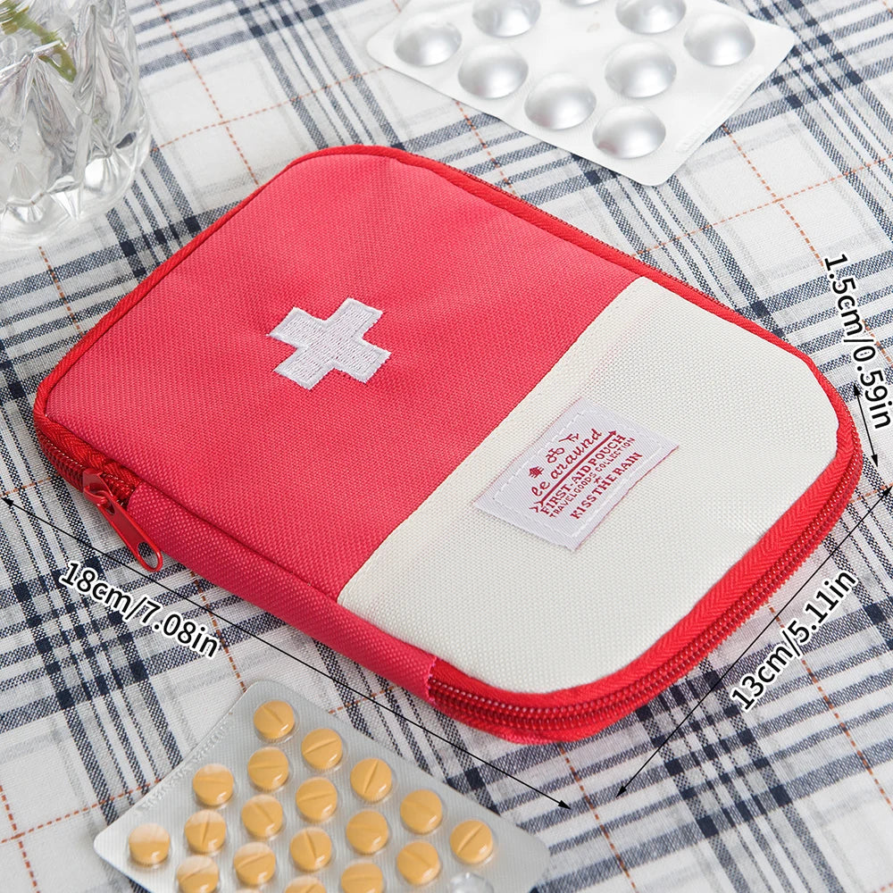 A pink and white compact travel medicine organizer bag is shown next to blister packs of pills on a plaid cloth.