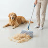 A person is using a long handle broom to sweep loose dog hair on a light-colored floor.