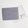 A gray genuine leather slim card holder wallet placed on a clear plastic background.