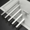 Ein Set moderner Edelstahl-Schubladengriffe diagonal auf einer grauen Oberfläche angeordnet.