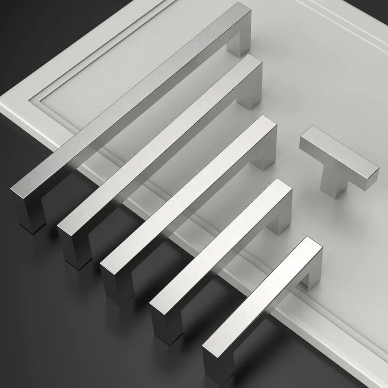 Ein Set moderner Edelstahl-Schubladengriffe diagonal auf einer grauen Oberfläche angeordnet.