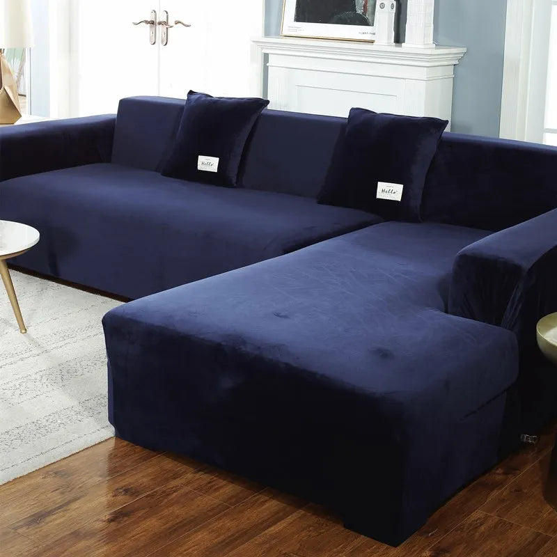 A dark navy blue plush velvet elastic sofa cover is shown on an L-shaped sectional sofa in a living room setting.