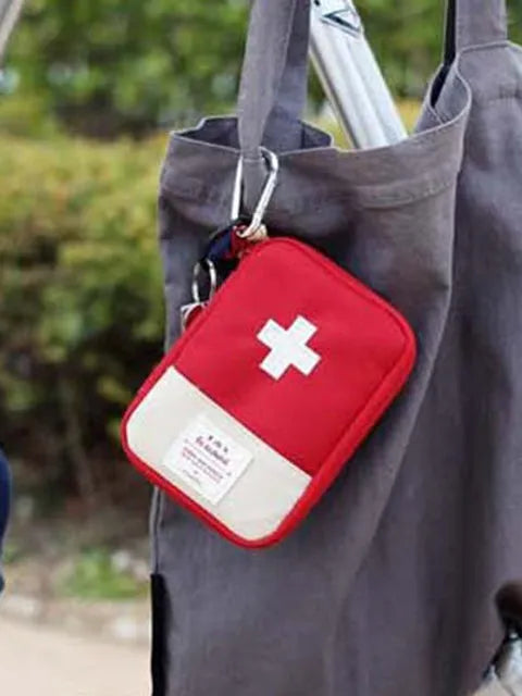 A red and white first aid kit pouch hangs from a gray fabric tote bag.