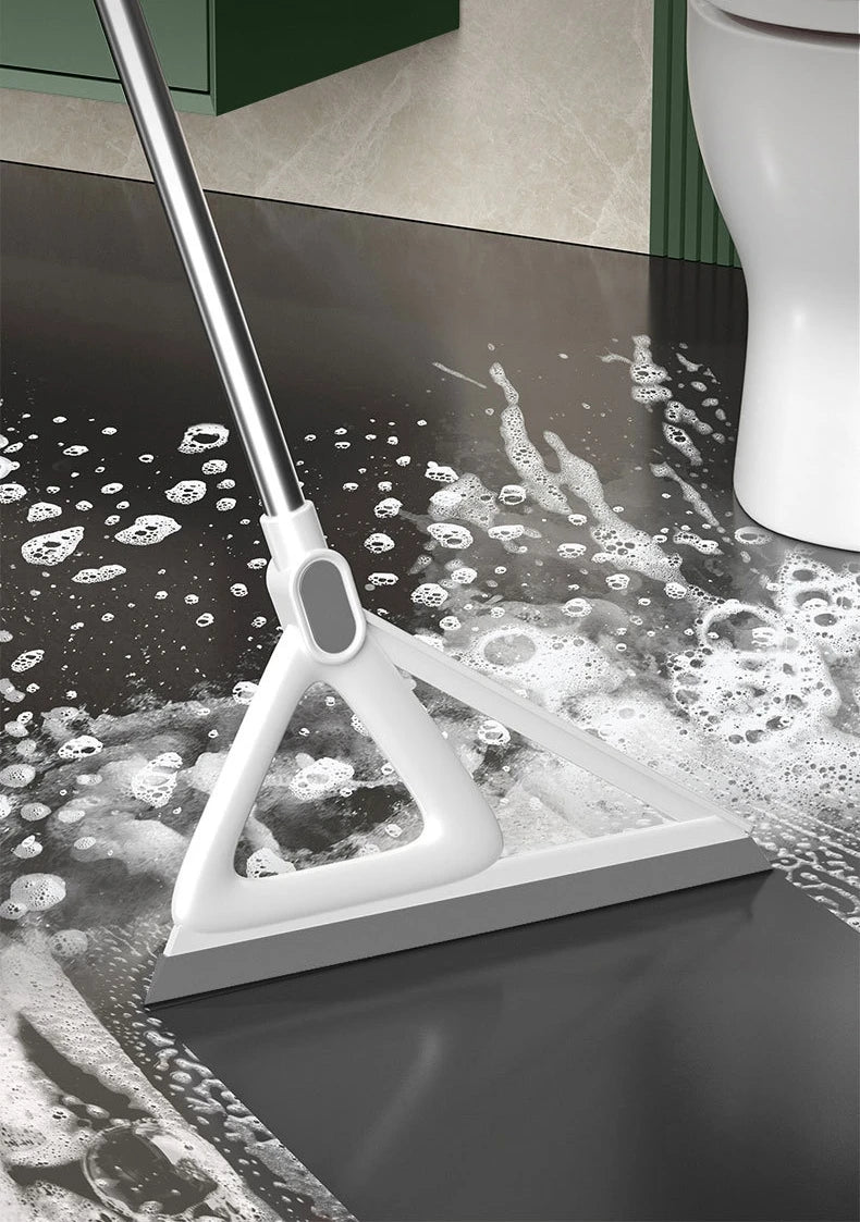 A white silicone squeegee broom is shown cleaning a dark floor surface with water and soap bubbles.