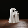 A white resin statue of a ghost making a middle finger gesture on a dark wooden surface.