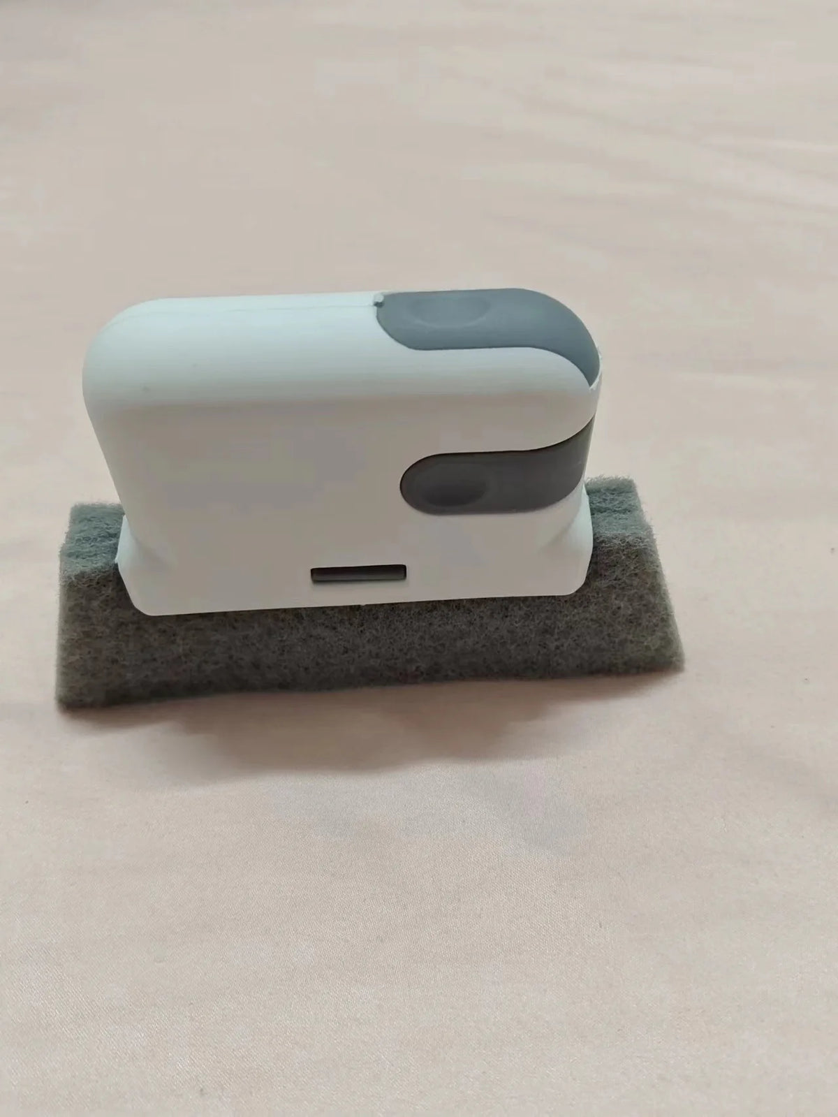 A white and gray multi-purpose crevice cleaning brush resting on a piece of gray foam.