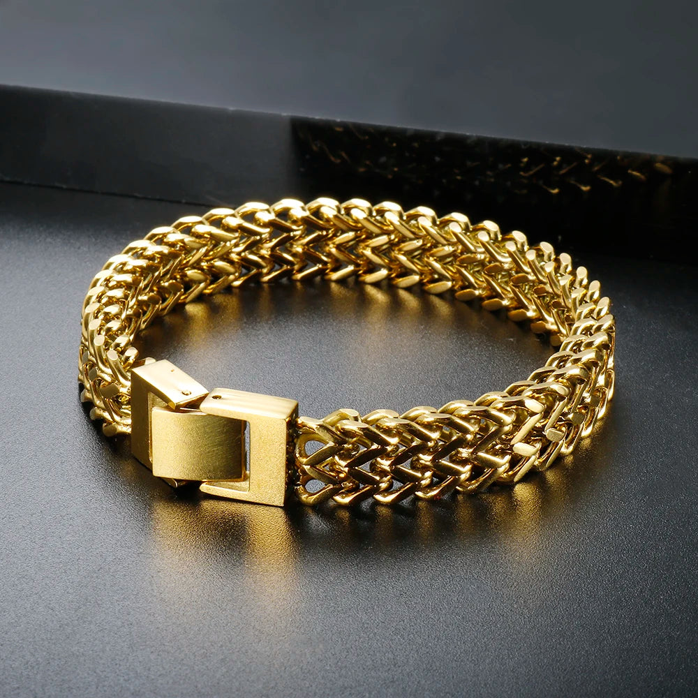 A chunky gold stainless steel link chain bracelet lying on a dark surface.
