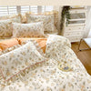 A floral duvet cover set featuring light beige and cream tones with ruffled edges, displayed on a bed.