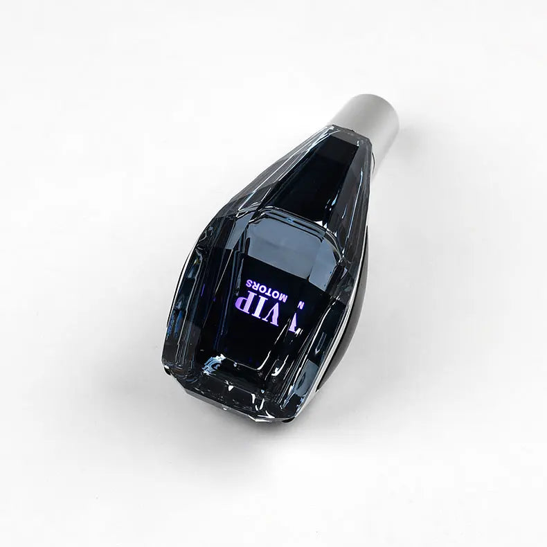 A close-up view of a black crystal gear shift knob with purple LED illumination and a silver cap.