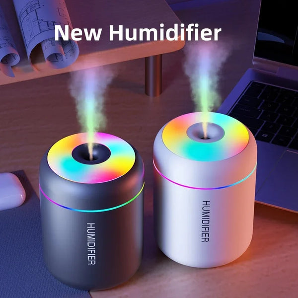 A white USB mini aromatherapy humidifier emitting a soft, multi-colored mist in an office setting.