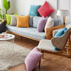 A collection of striped velvet corduroy cushion covers in various shades of pink, purple, orange, and green displayed on a so