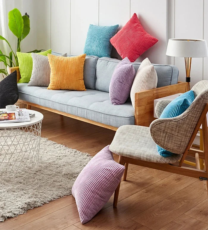A collection of striped velvet corduroy cushion covers in various shades of pink, purple, orange, and green displayed on a so