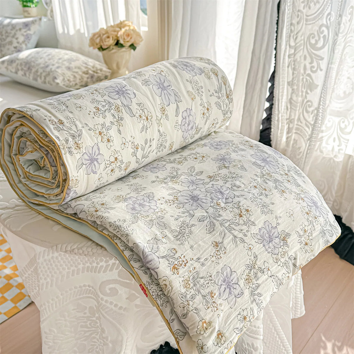 A rolled-up pastoral print lightweight summer quilt with floral patterns displayed on a white surface.